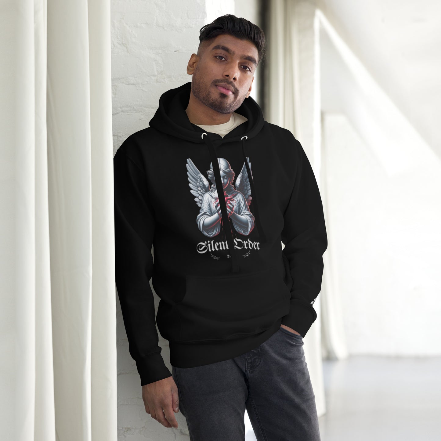 Man wearing a black hoodie with a graphic design and text, standing against a white wall.