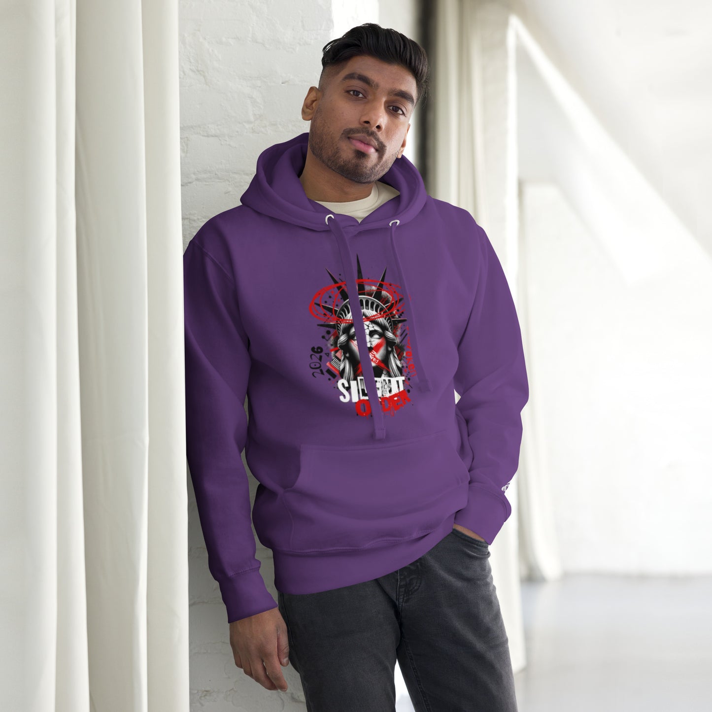 Man wearing a purple hoodie with a graphic design, standing against a white wall.