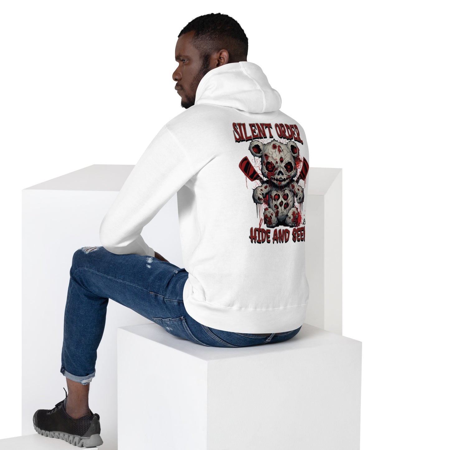 Person wearing a white hoodie with a graphic design on the back, sitting on a white cube.