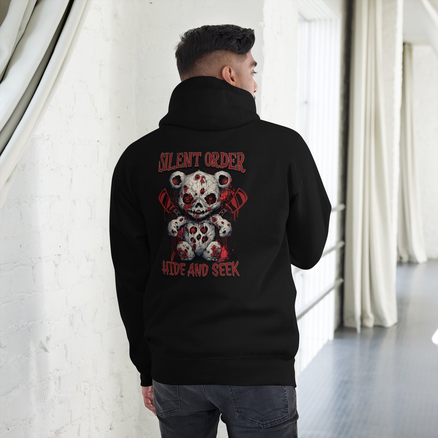 Person wearing a black hoodie with a graphic design on the back, standing in a room with white walls and curtains.
