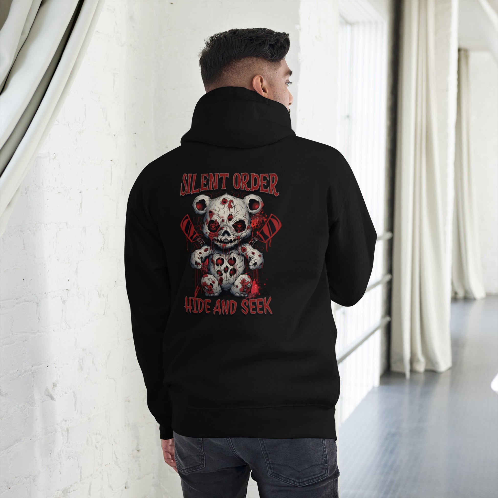 Person wearing a black hoodie with a graphic design on the back, standing in a room with white walls and curtains.